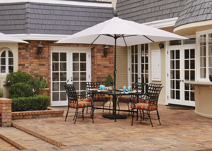 white market umbrella over a small outdoor dining table on a brick patio