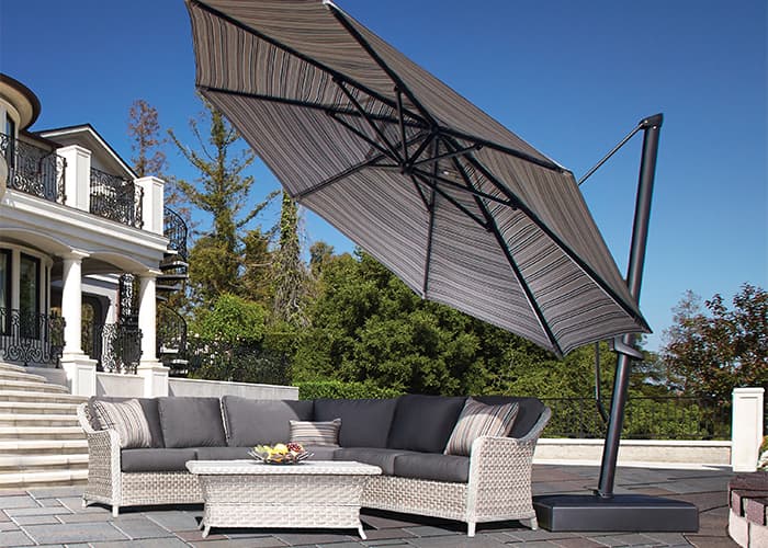 large grey striped cantilever umbrella over a large outdoor sofa on the stone patio of an upscale, large house with black iron railings